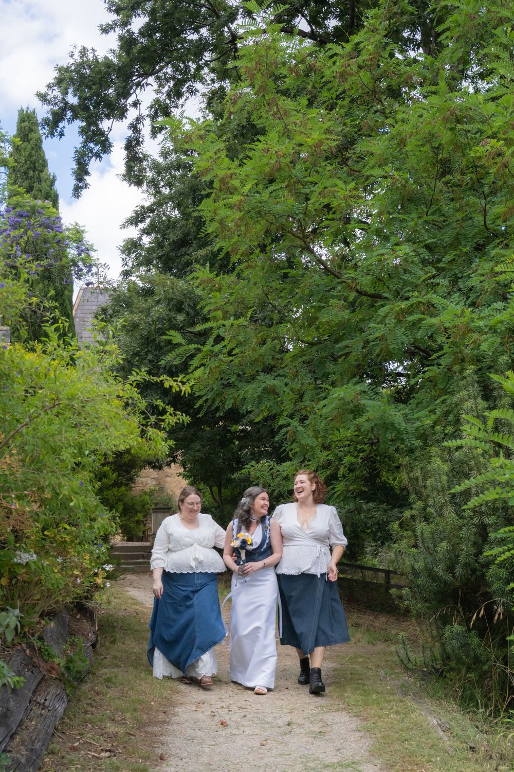 A group gathers on a garden path surrounded by lush green trees and foliage on a sunny day.