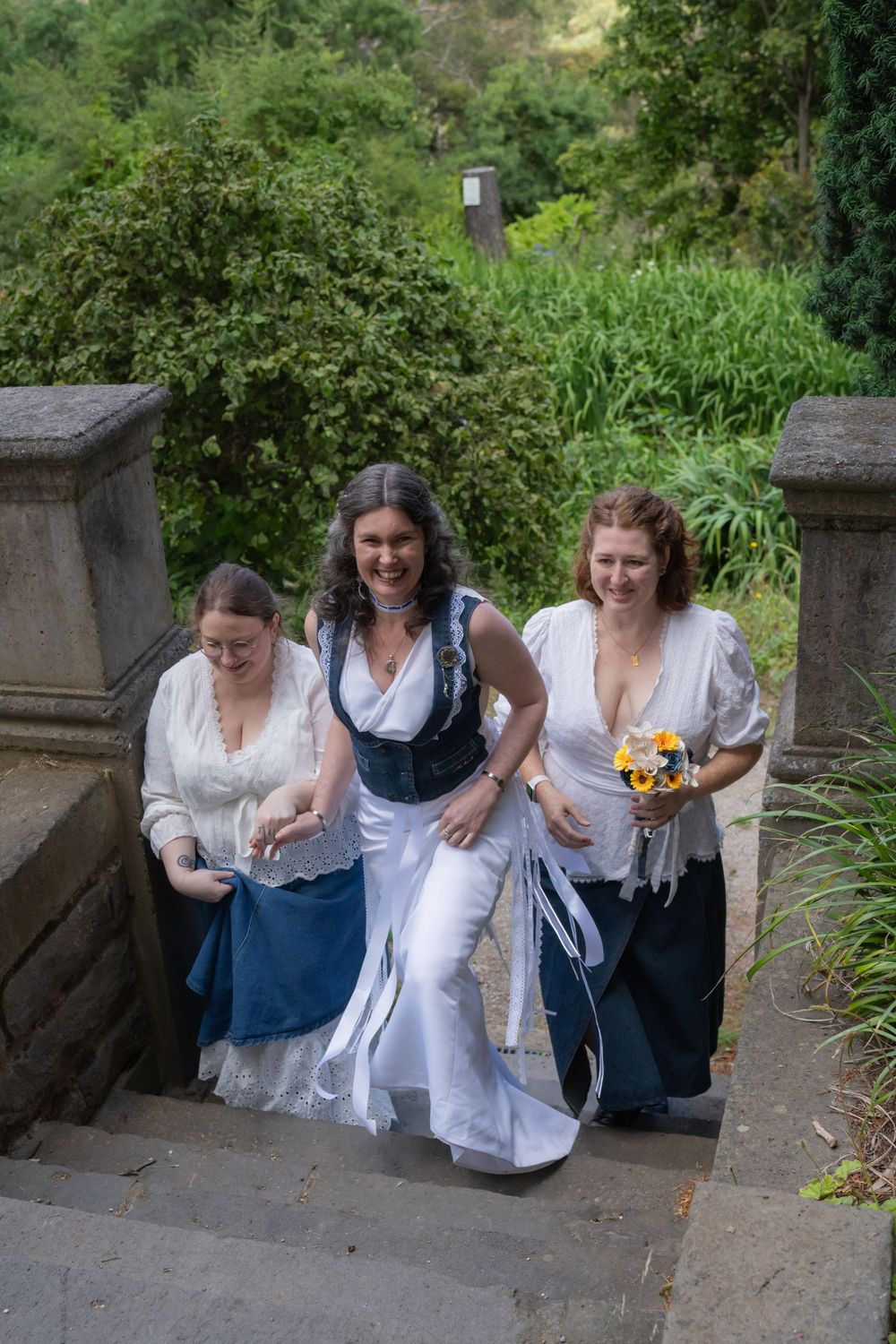 Three people in period costumes lean over stone bridge railing looking down at something below.