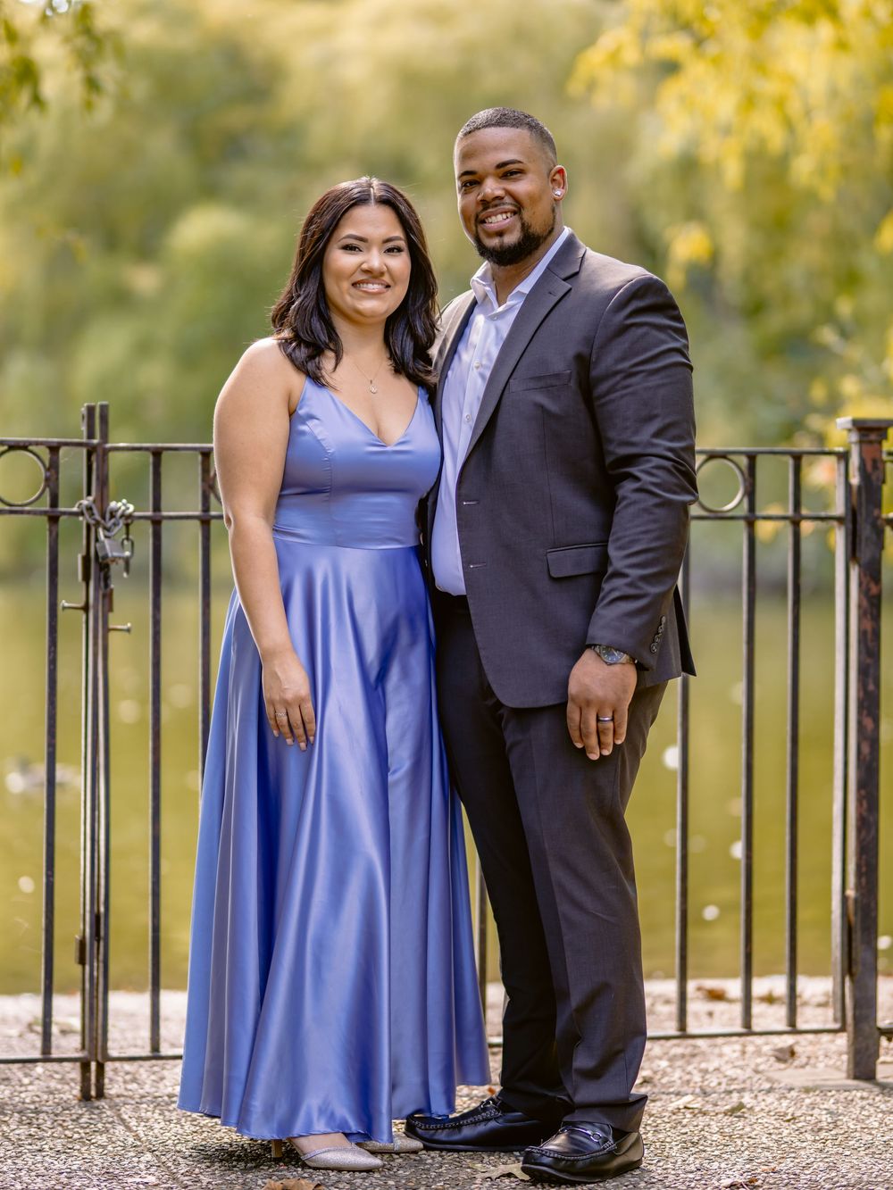 A couple poses together at an outdoor venue, wearing formal attire with a periwinkle blue gown and dark suit beautiful engagement shoot