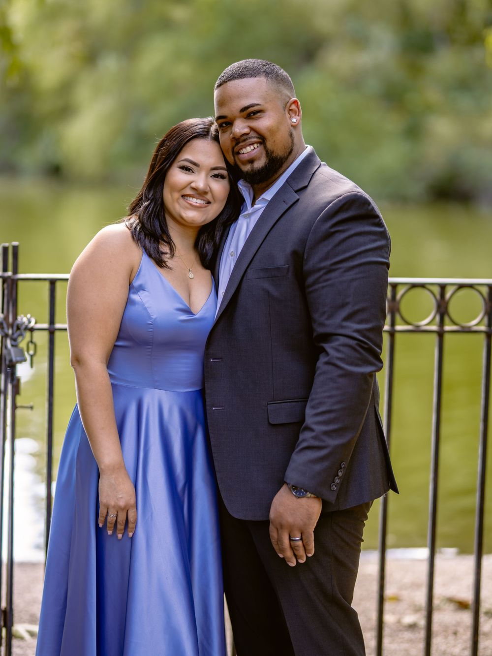 A couple shares a romantic moment by a wrought iron railing, with the woman in blue and man in dark suit beautiful engagement shoot