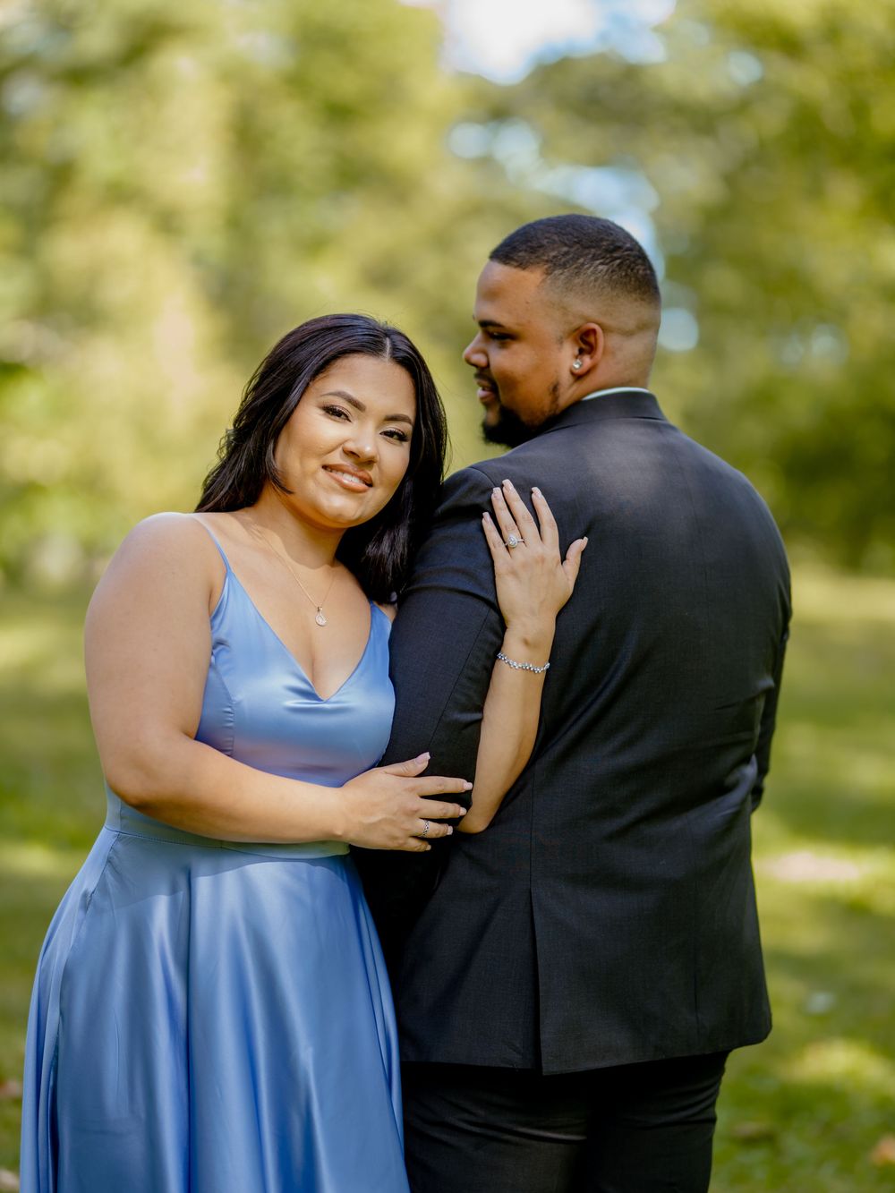 A couple shares an intimate moment outdoors as they embrace while wearing formal attire in a sun-dappled setting beautiful engagement shoot