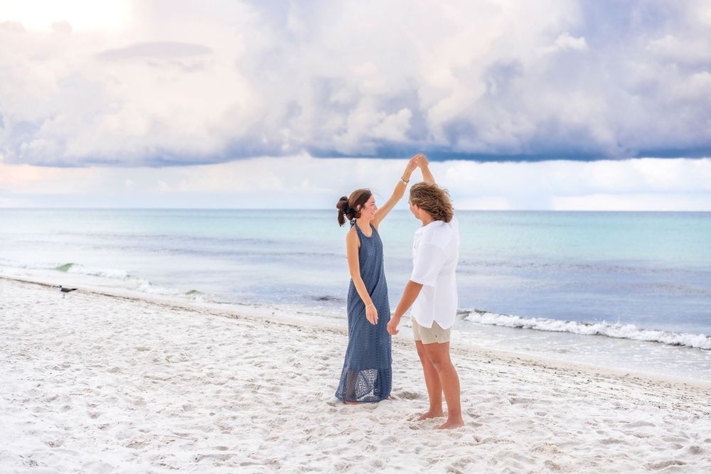 Couple embracing on a white sandy beach with turquoise ocean waters and cloudy sky in the background.