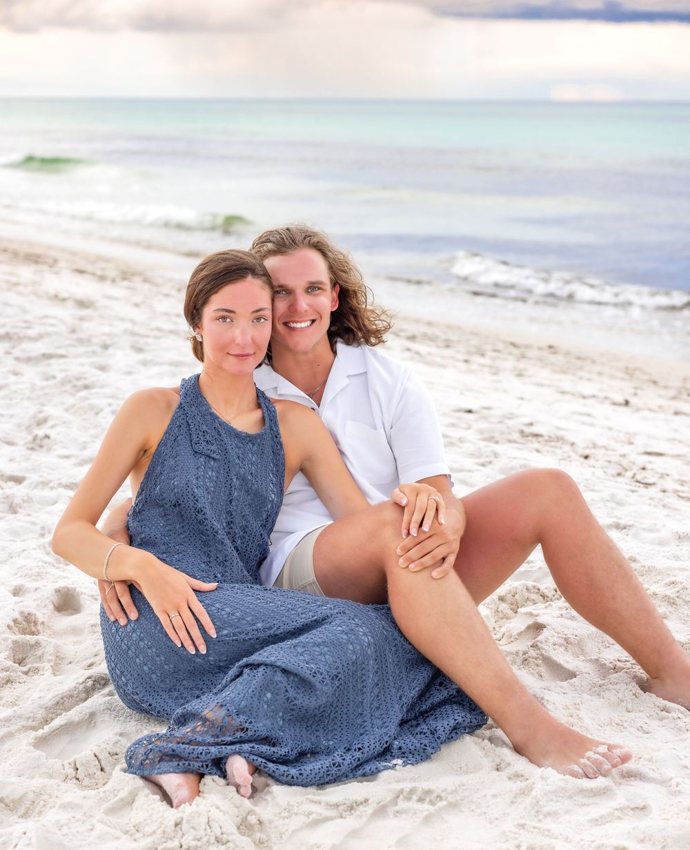 A couple relaxes together on a pristine white sandy beach with turquoise ocean waters in the background.