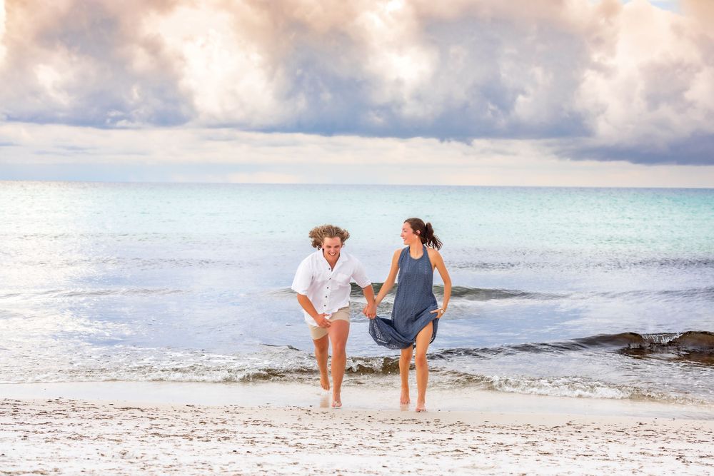 Couple walking along a misty beach shore while waves crash in a romantic oceanside setting.
