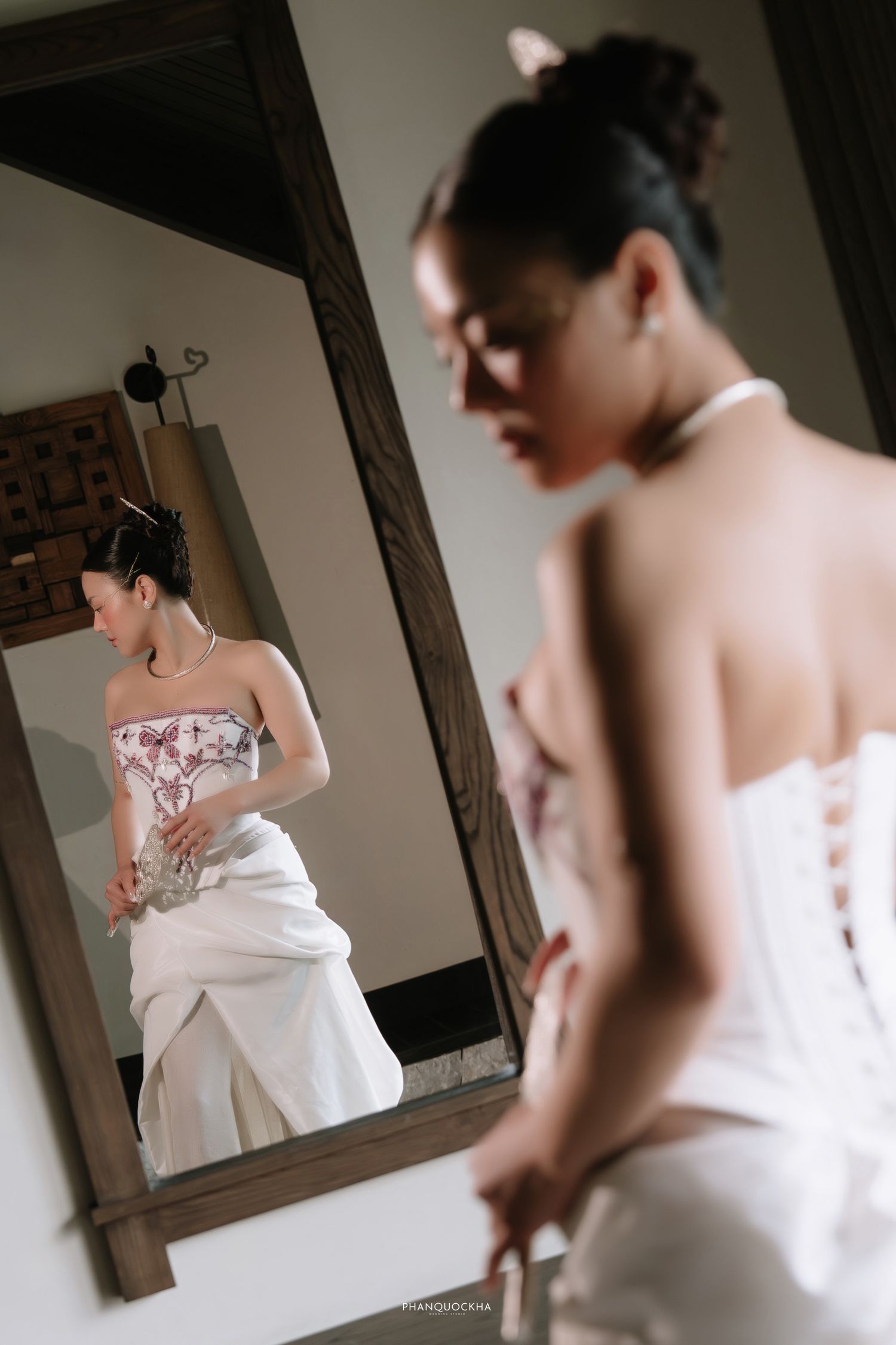 Bride in white strapless embroidered wedding gown adjusting dress before mirror.