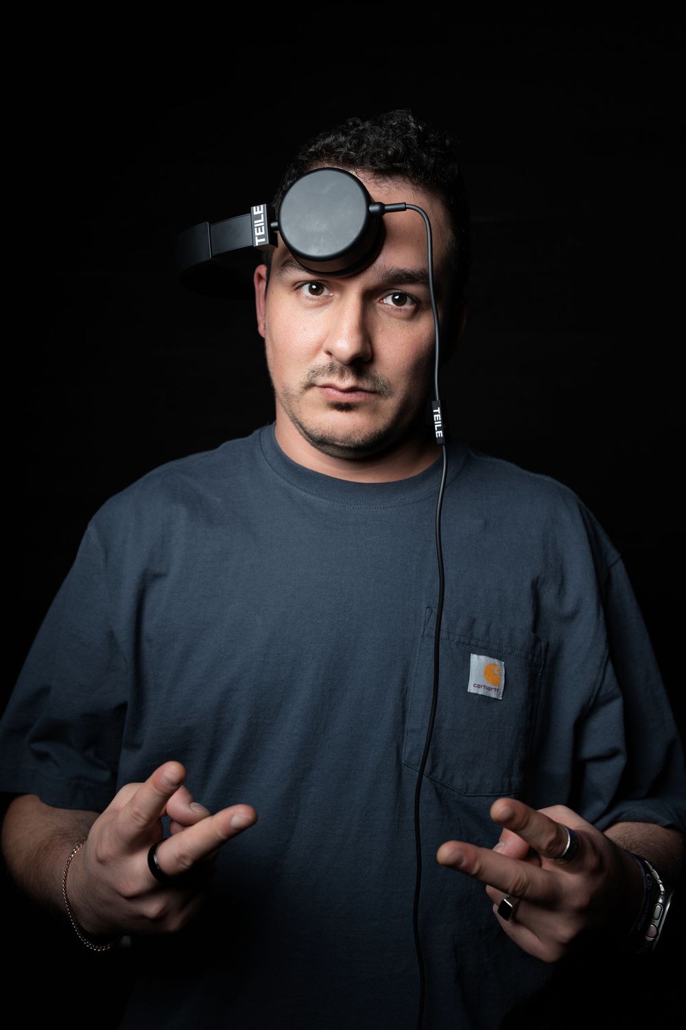 Person in dark navy t-shirt makes hand gestures against black background in dramatic lighting sequence.