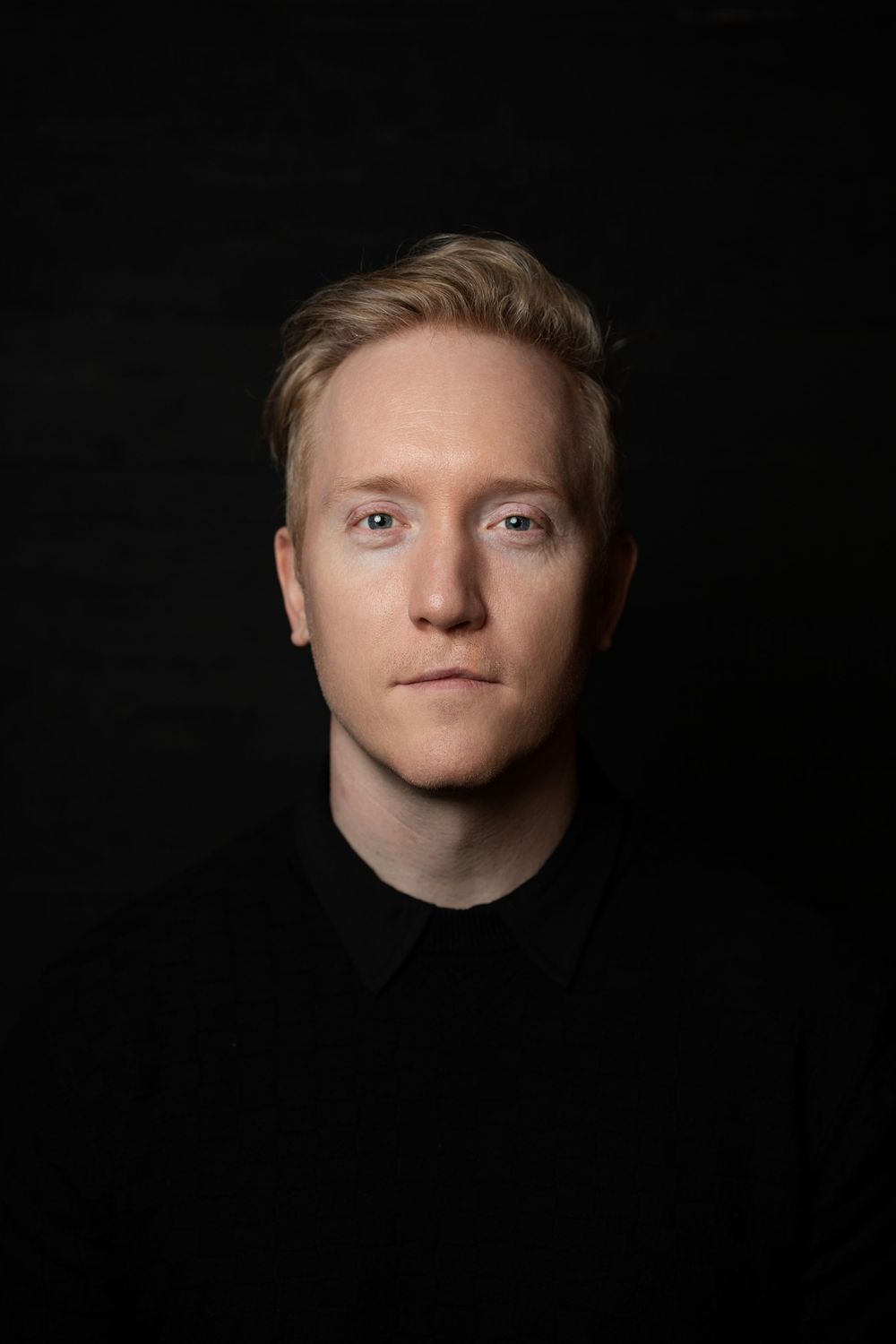 Portrait of someone wearing black clothing against a dark background with dramatic lighting.
