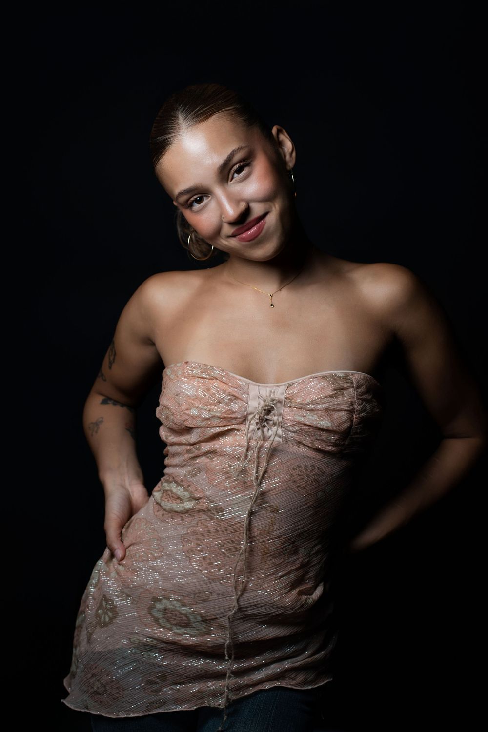 Portrait against dark background shows someone wearing a strapless beige lace top and denim jeans.