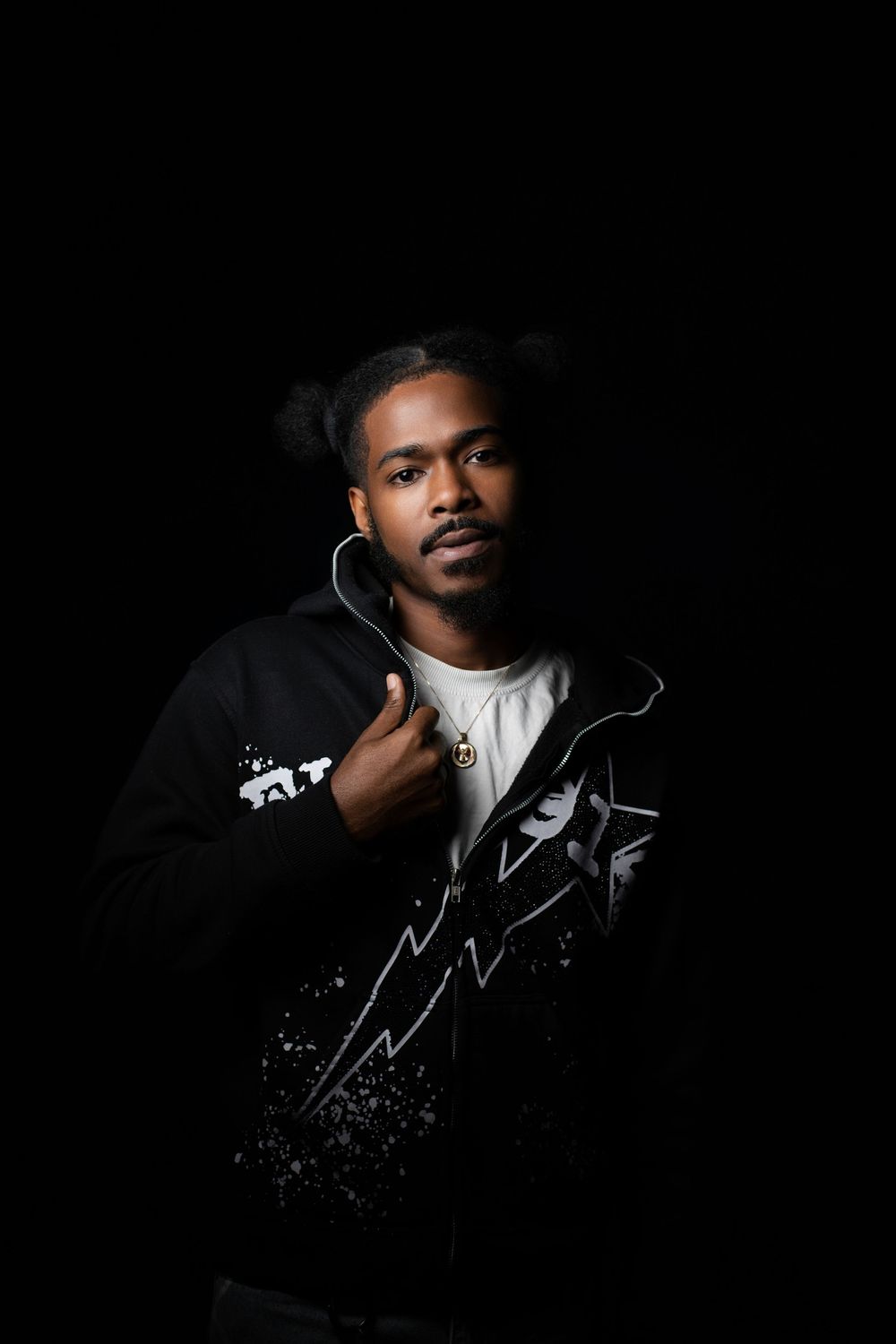 Dramatic portrait against black background wearing black jacket with white t-shirt underneath, creating striking contrast.