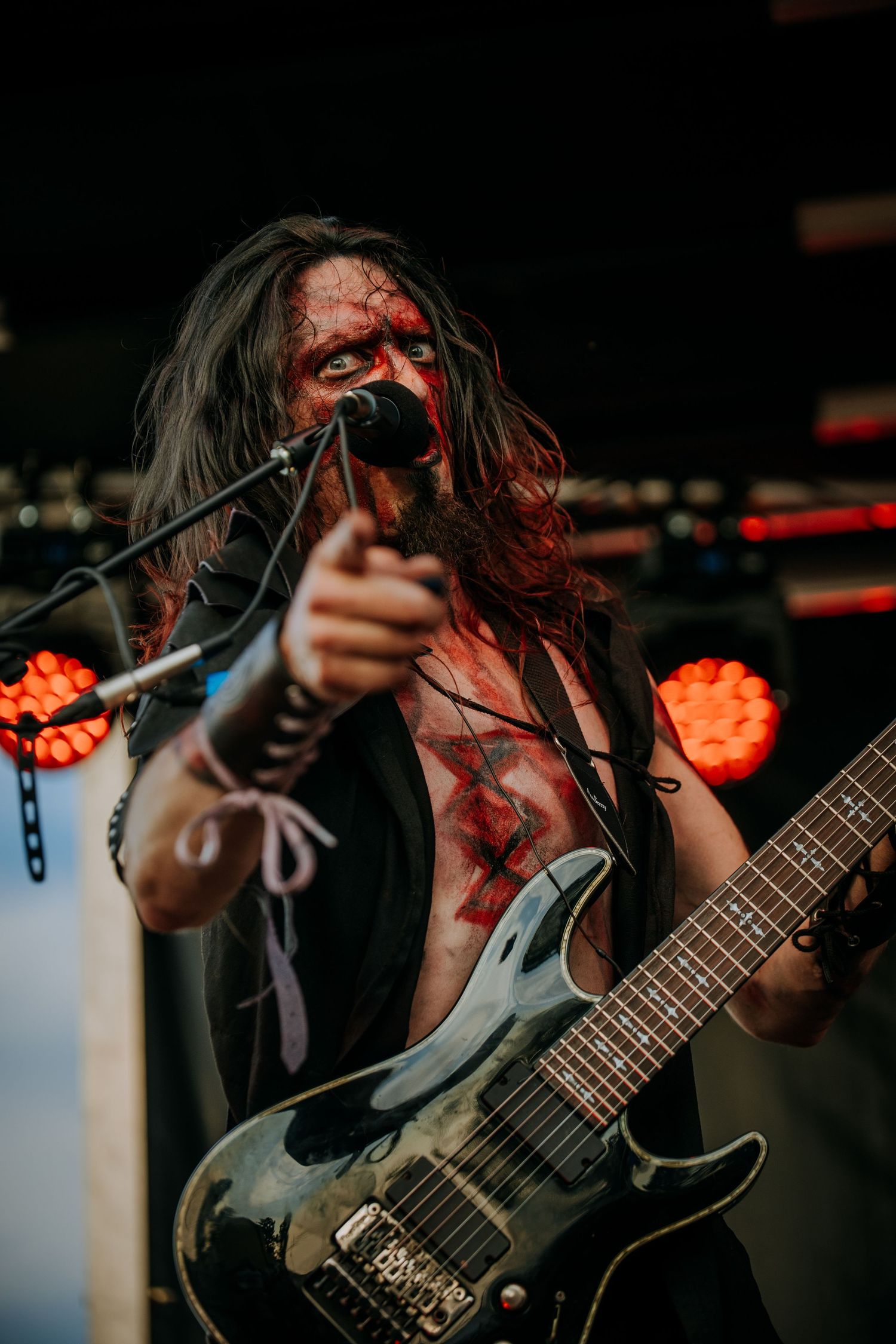 Energetic performer plays electric guitar on stage with dramatic red lighting and intense expression during live performance.