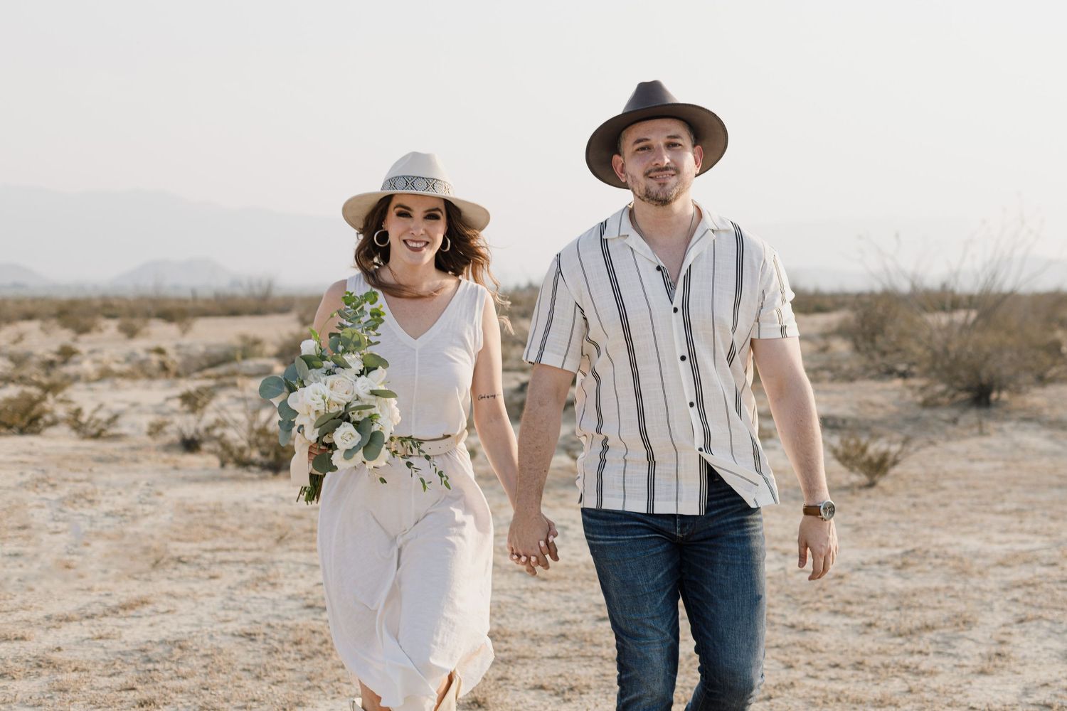 Couple walking hand in hand through desert landscape in casual bohemian style.