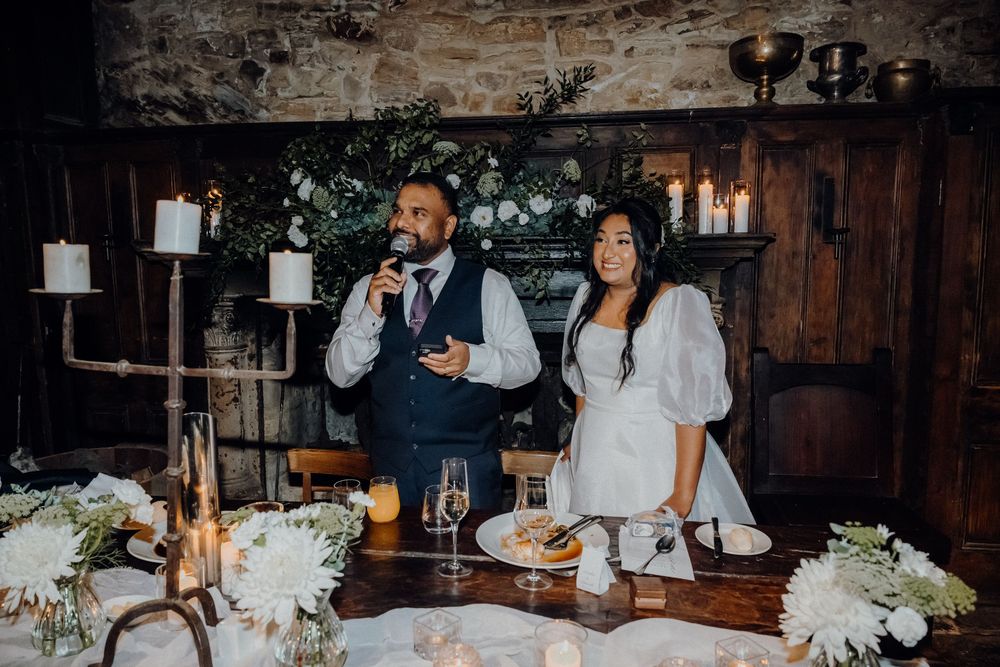 Reception guests celebrate at a rustic indoor wedding venue with wood panels and white floral centerpieces.