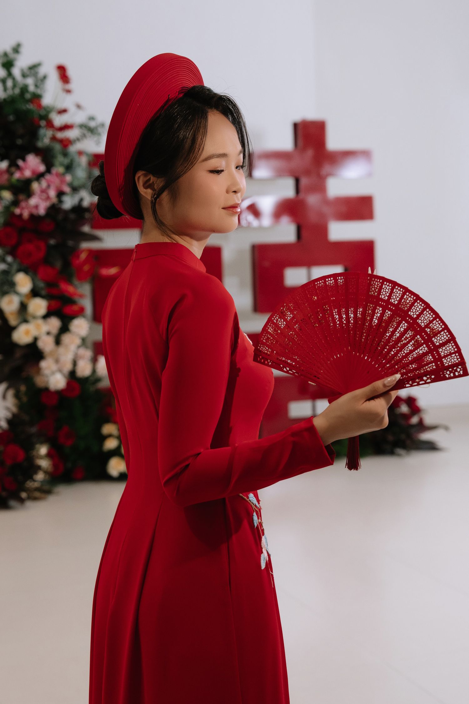 Vietnamese bride in red ao dai and beret holding red fan with double happiness symbol.
