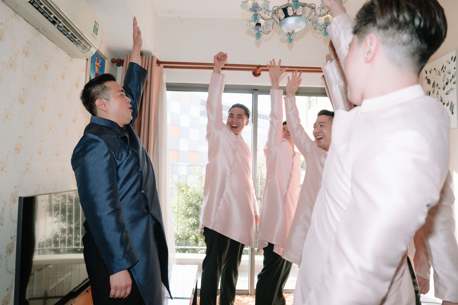 Groom and groomsmen in pink barong shirts celebrating with raised hands indoors.