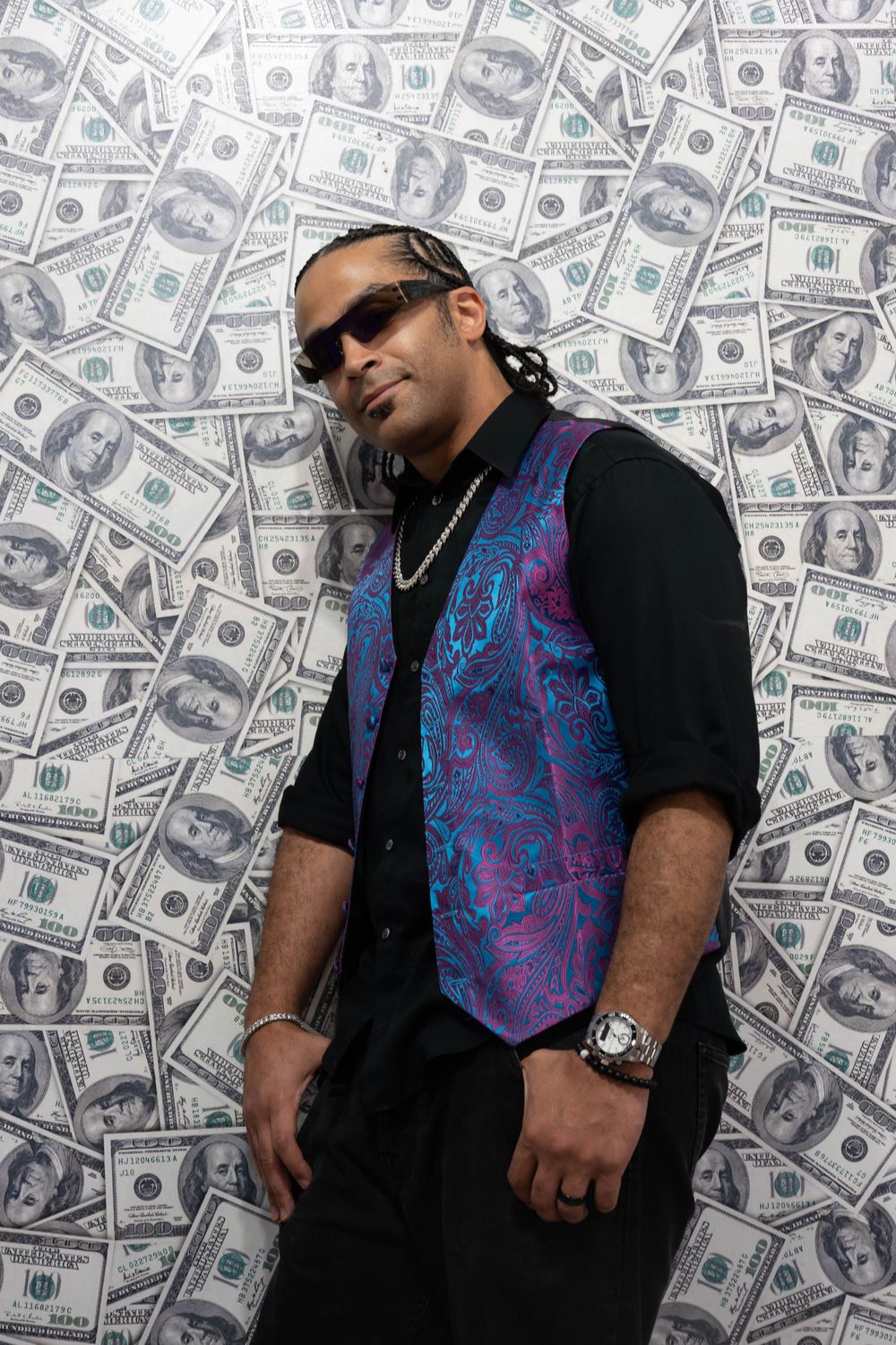 Man in purple paisley vest and sunglasses poses confidently against a backdrop of hundred dollar bills.