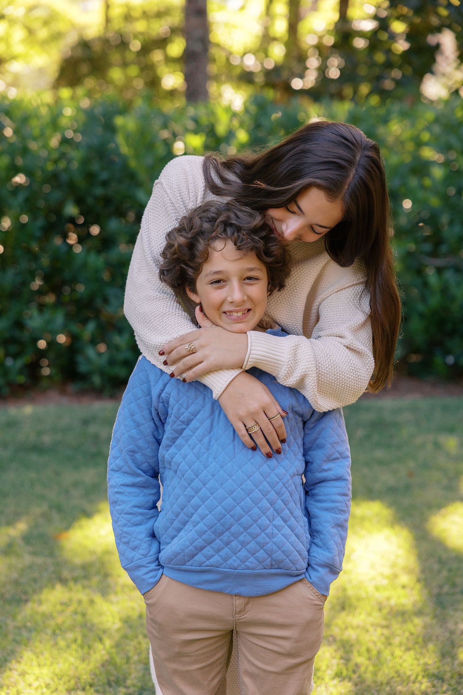 Family wearing coordinating fall clothing poses casually on grassy field at sunset.