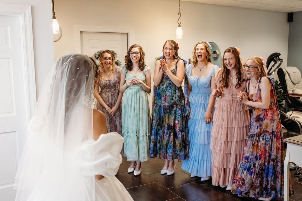 Bridesmaids wearing colorful floral and pastel dresses stand together in a row at a wedding celebration.