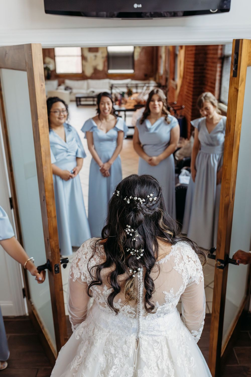 A back view of someone in a white lace wedding dress with bridesmaids in light blue dresses standing in front.