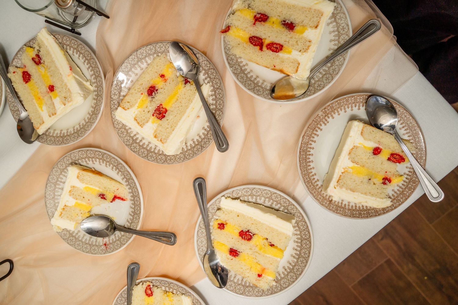 Several plates of creamy white tres leches cake topped with cherries and yellow garnish sit on a wooden table.