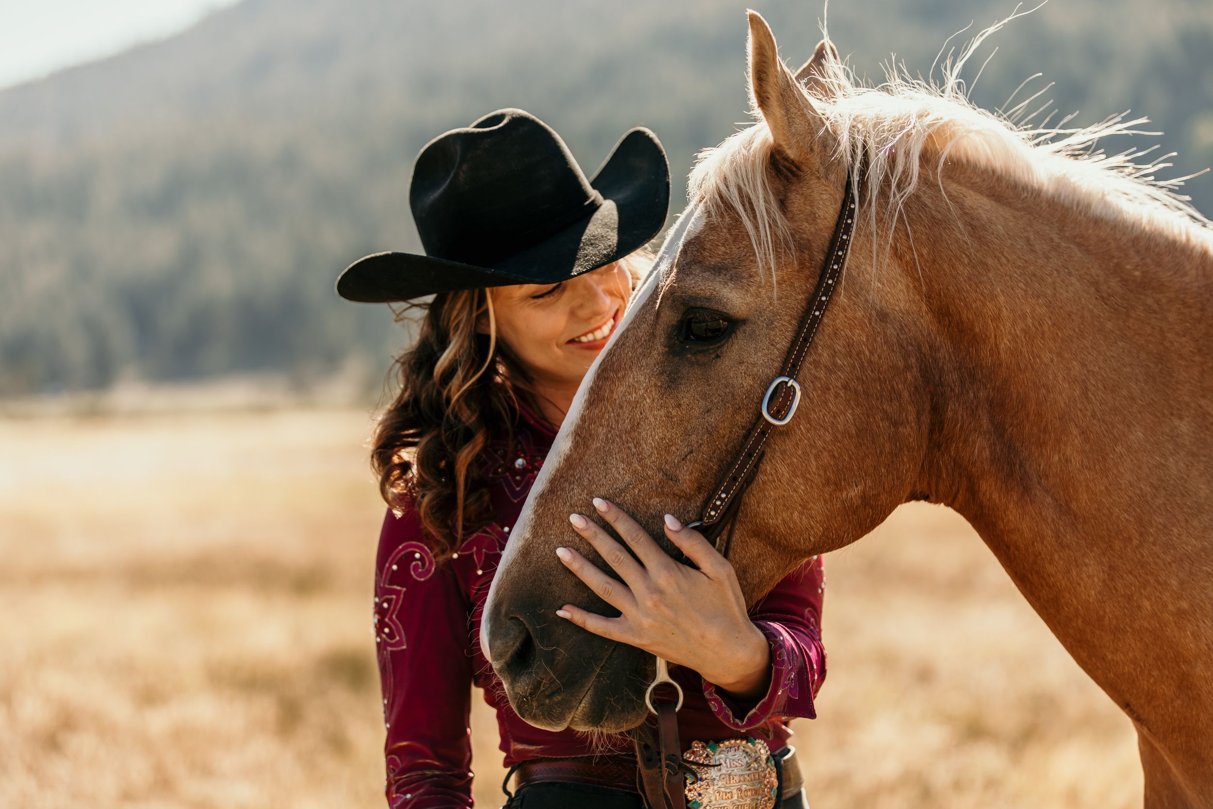 A close-up moment between a brown horse and rider against a mountain backdrop.