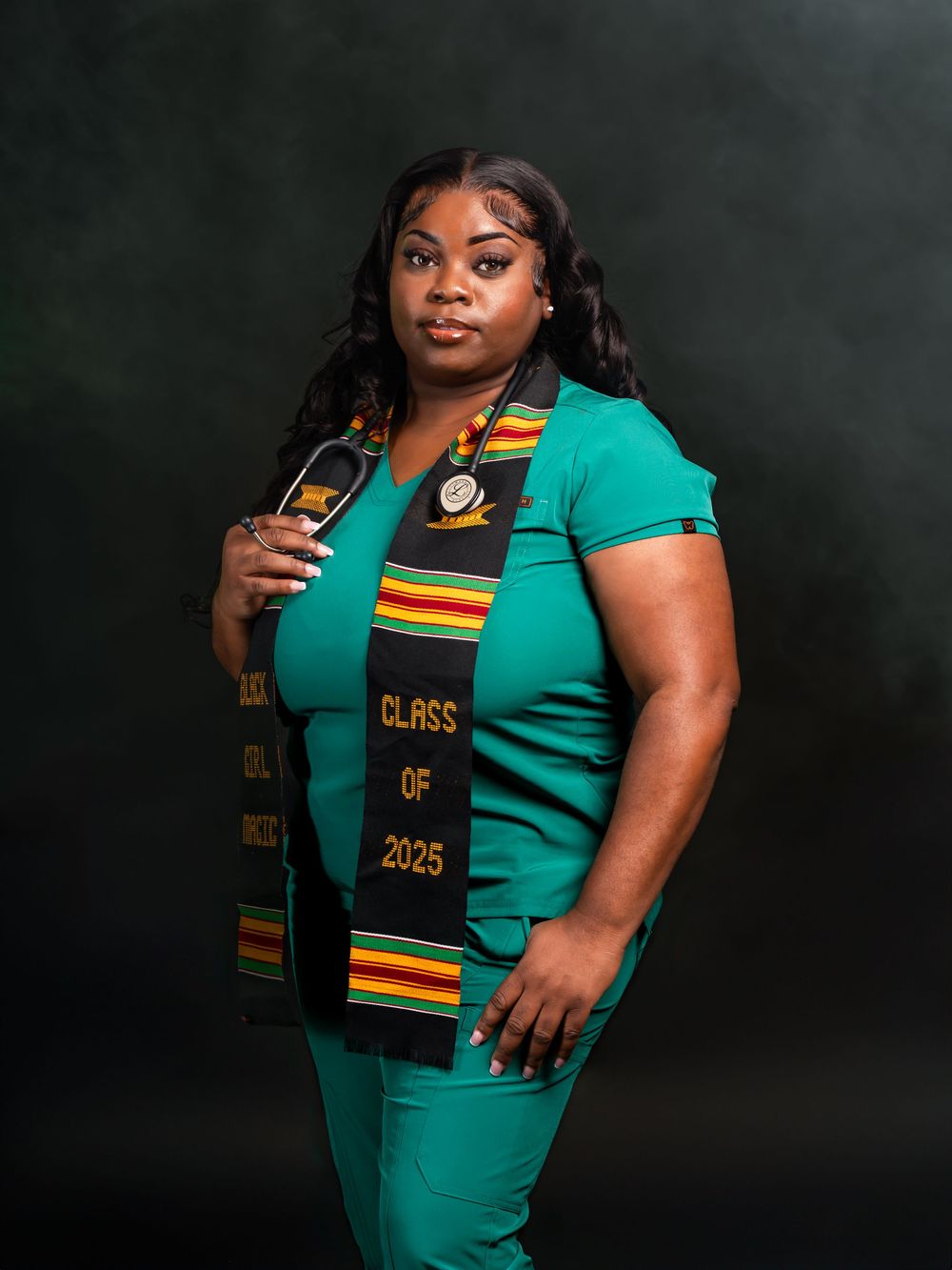 Graduate wearing green attire and Class of 2023 graduation stole poses against dark background.