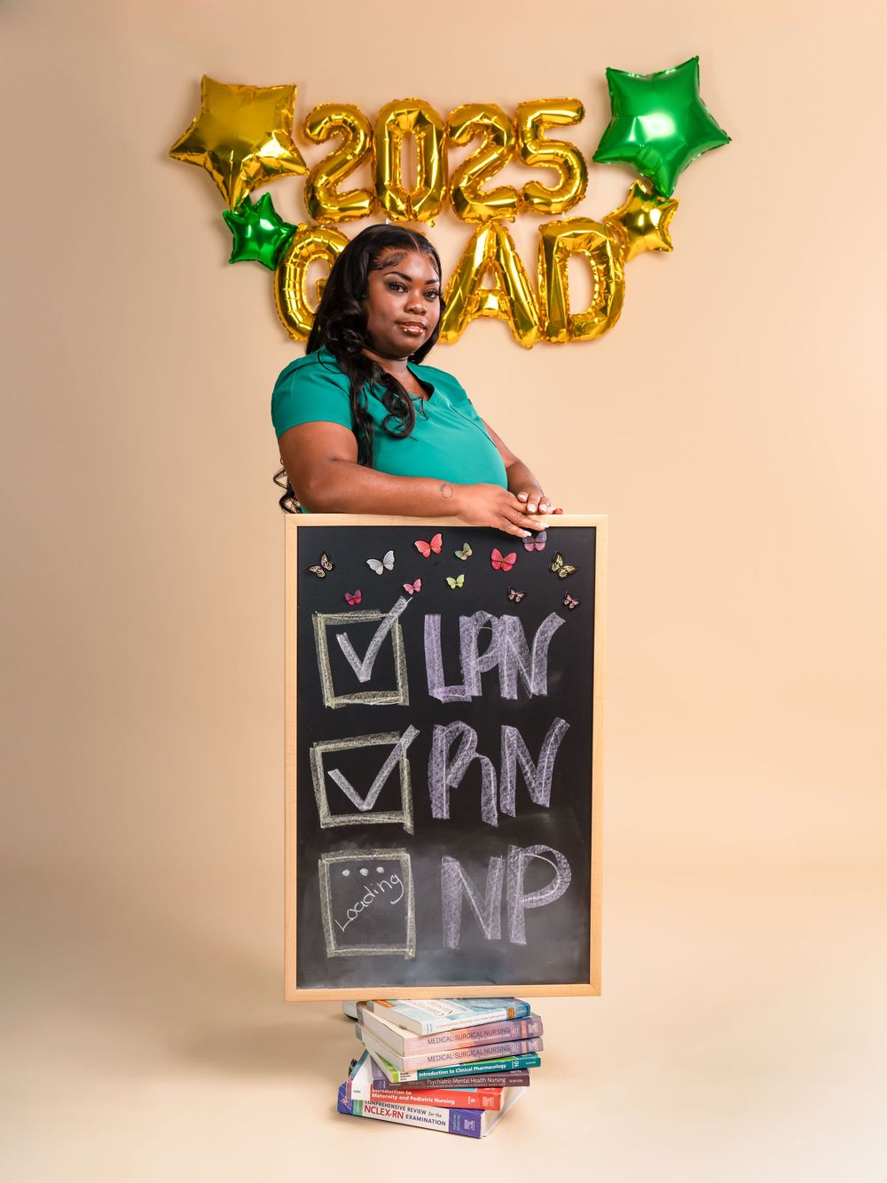 Graduate with chalkboard checklist posing against backdrop with gold 2025 balloons.