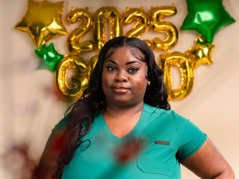 Healthcare professional in teal uniform celebrating with gold graduation balloons.