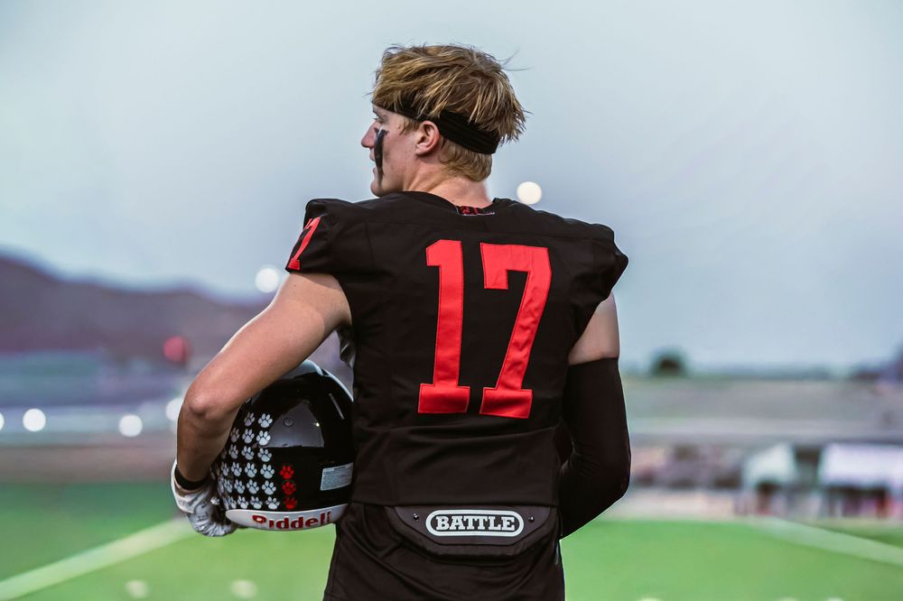 Football player holding his helmet and looking off left screen