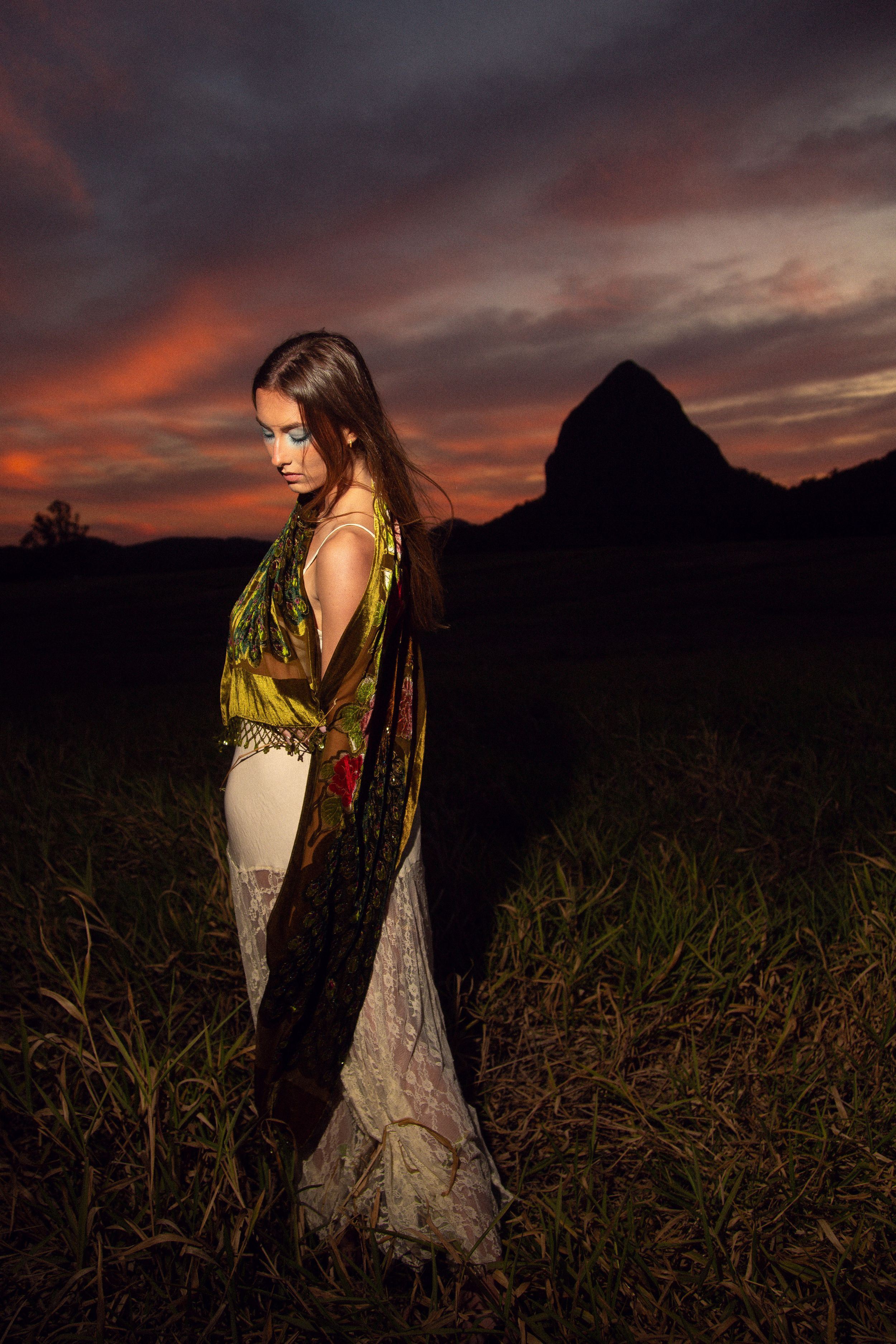 Dramatic sunset photo shoot in a field with dramatic orange and purple sky creating moody silhouettes against tall grass.