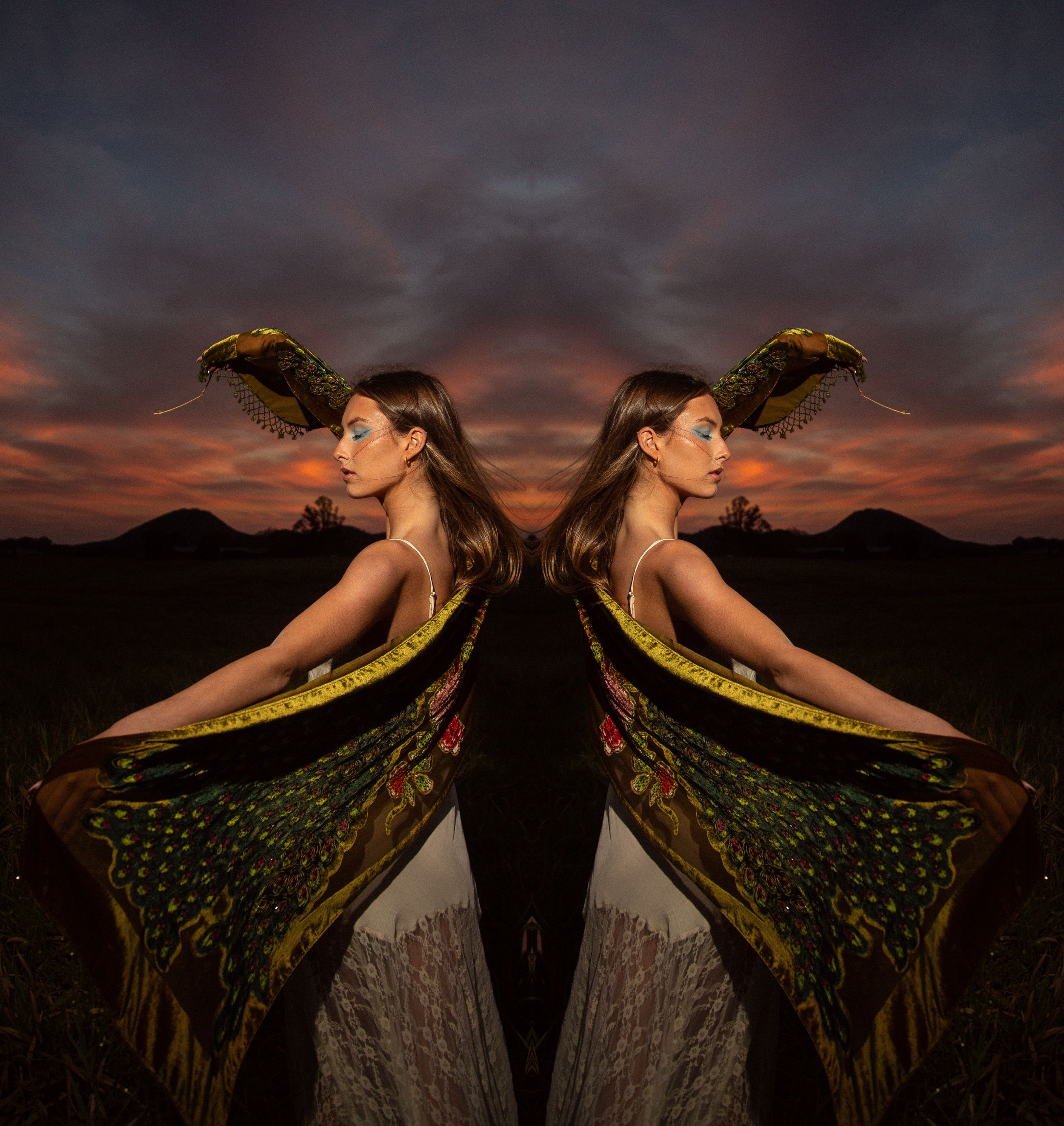 A dancer in flowing green fabric poses dramatically against a vibrant sunset sky with mountains in the background.