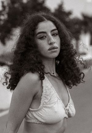 Black and white portrait showcasing dramatic curly hair and vintage-style fashion.