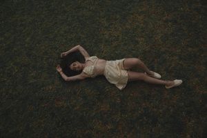 A person lying on dark grass wearing a light-colored dress creates a dreamy artistic composition.