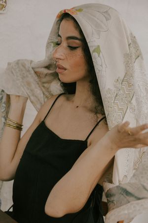 Dreamy portrait with floral headscarf and black camisole against textured white background.