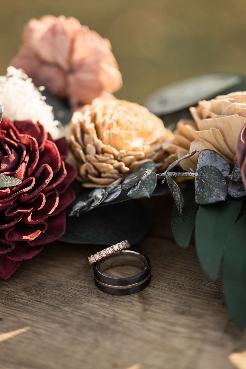 Close-up of wedding rings and burgundy roses arranged on a rustic wooden surface.