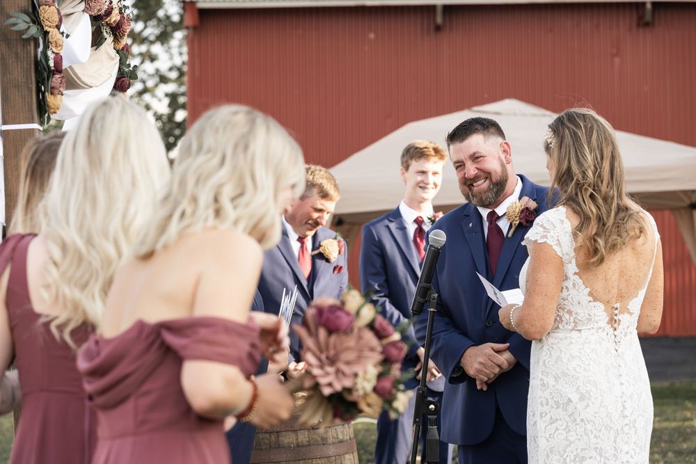 Wedding party celebrates and laughs together outdoors in front of a rustic red barn.