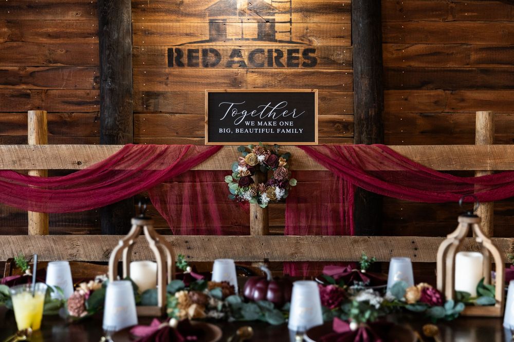 Rustic wedding reception venue with wooden walls, red drapery, and elegant table settings illuminated by soft lighting.