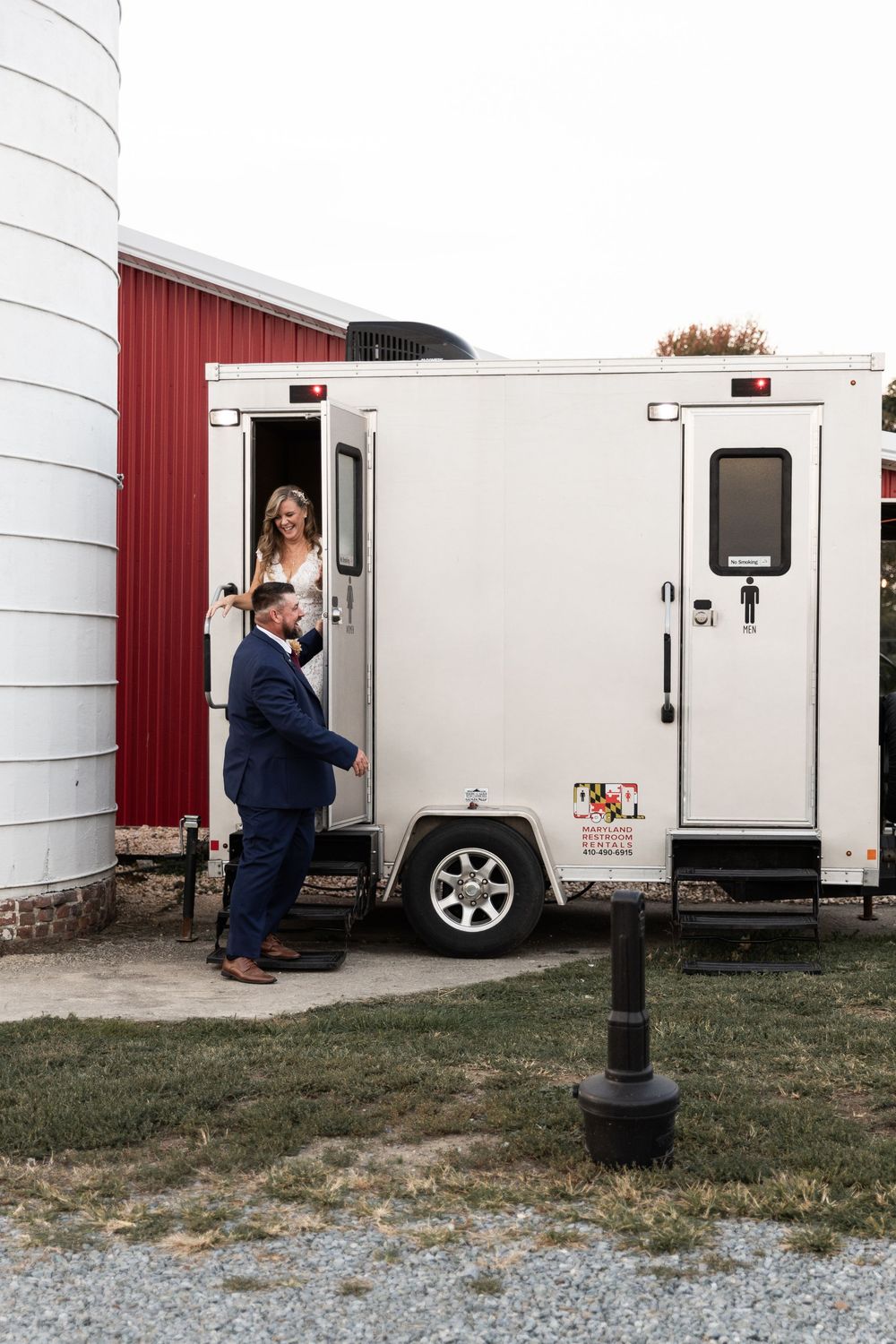 White trailers parked outside a red barn on a gravel surface.