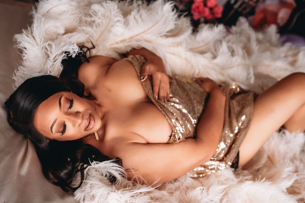 A woman in a romantic boudoir pose lies among soft white feathers and delicate lace.