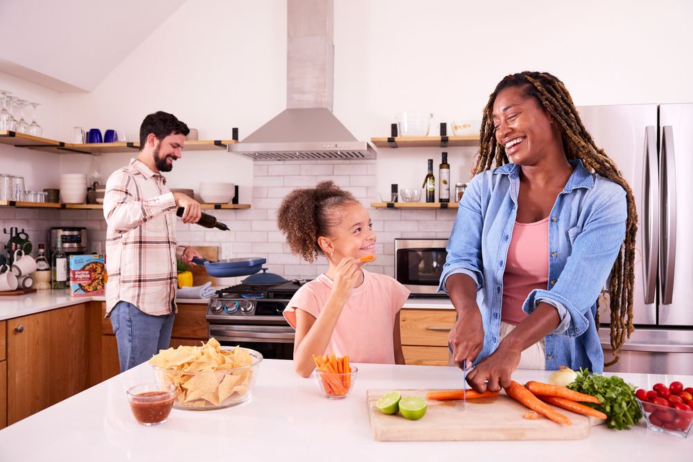 Friends enjoying food and conversation in bright modern kitchen setting.