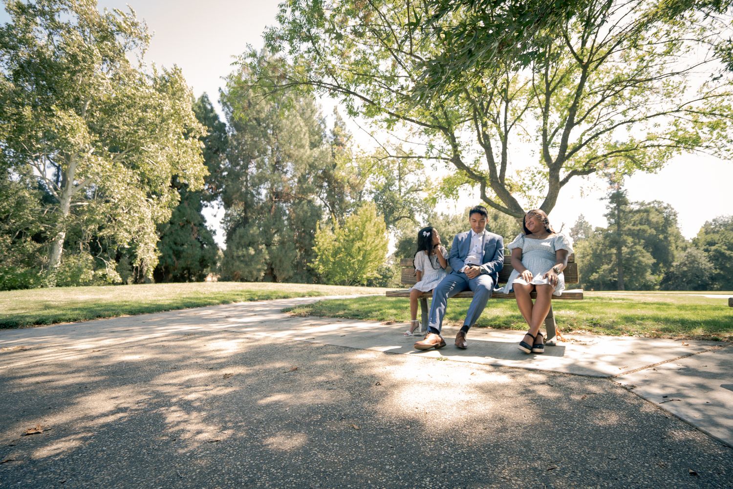 People enjoying a sunny day together in a peaceful park setting with lush trees and a dirt pathway.