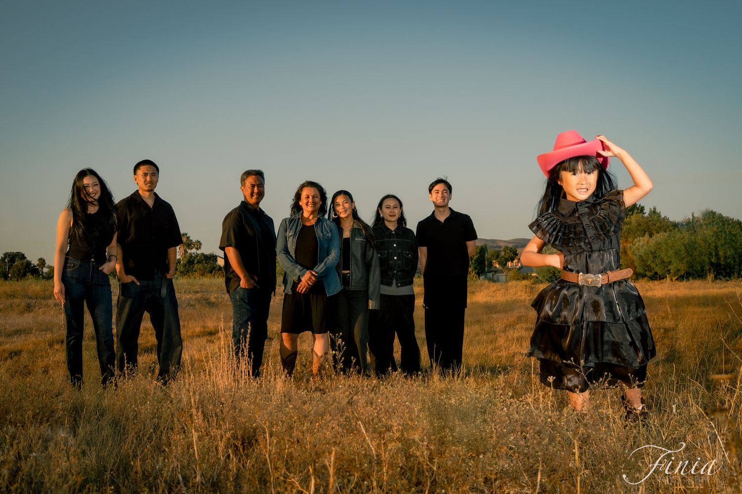 A group of people stand together in a golden field at sunset creating a silhouette against the warm sky.