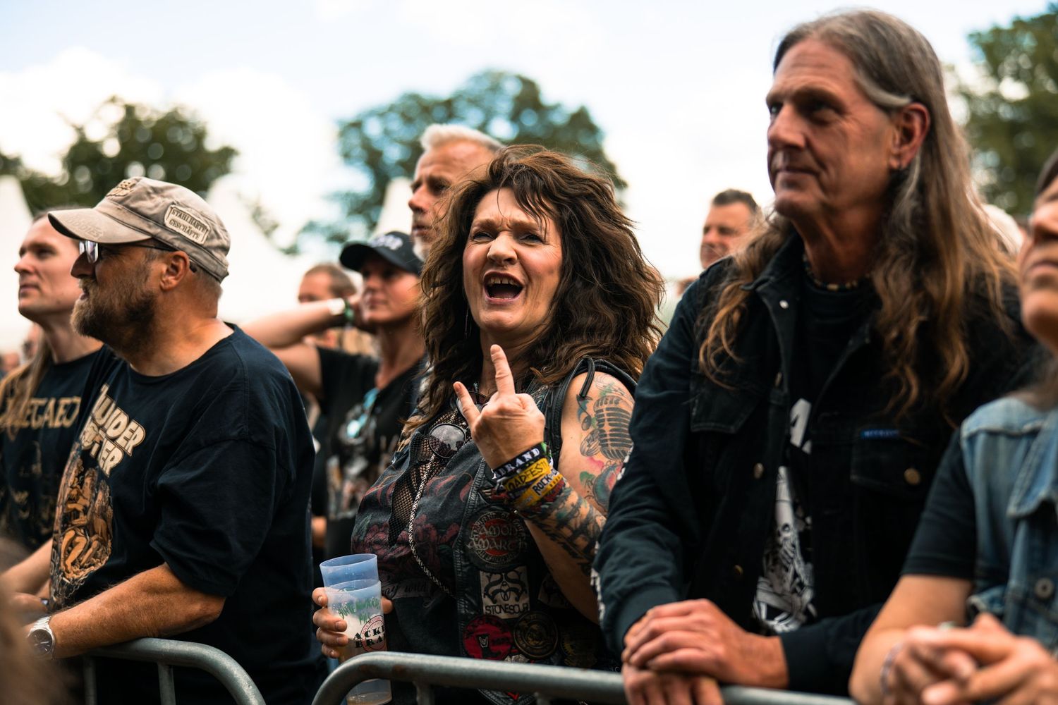 Energetic crowd of metal music fans cheering and headbanging at an outdoor concert festival.