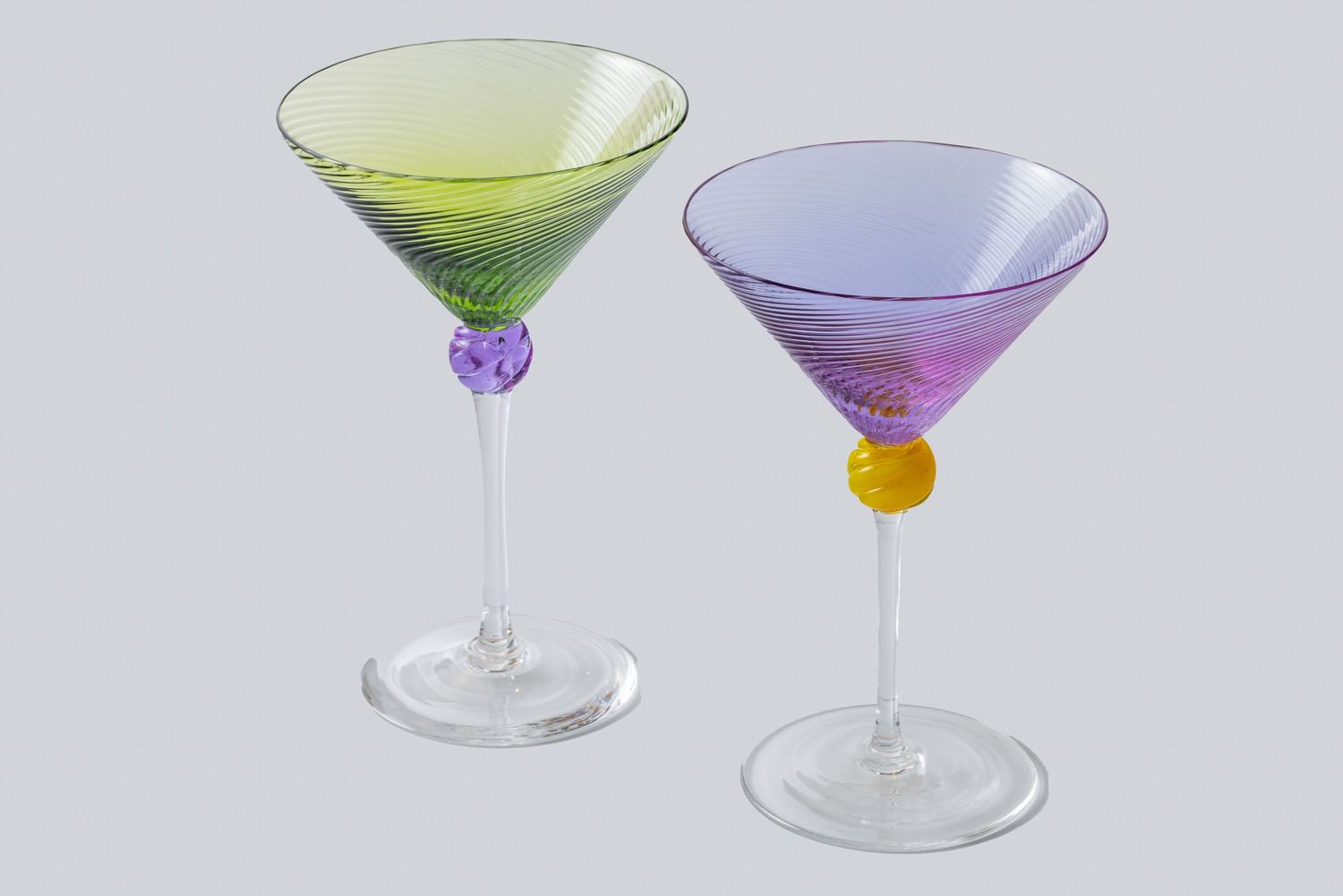 Two elegant martini glasses with colorful stems, one filled with green liquid and one with purple-tinted glass.