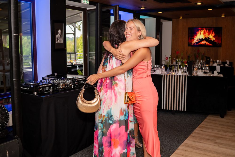 Two people embrace warmly while dancing in a festive indoor venue with colorful lighting and decorative elements.