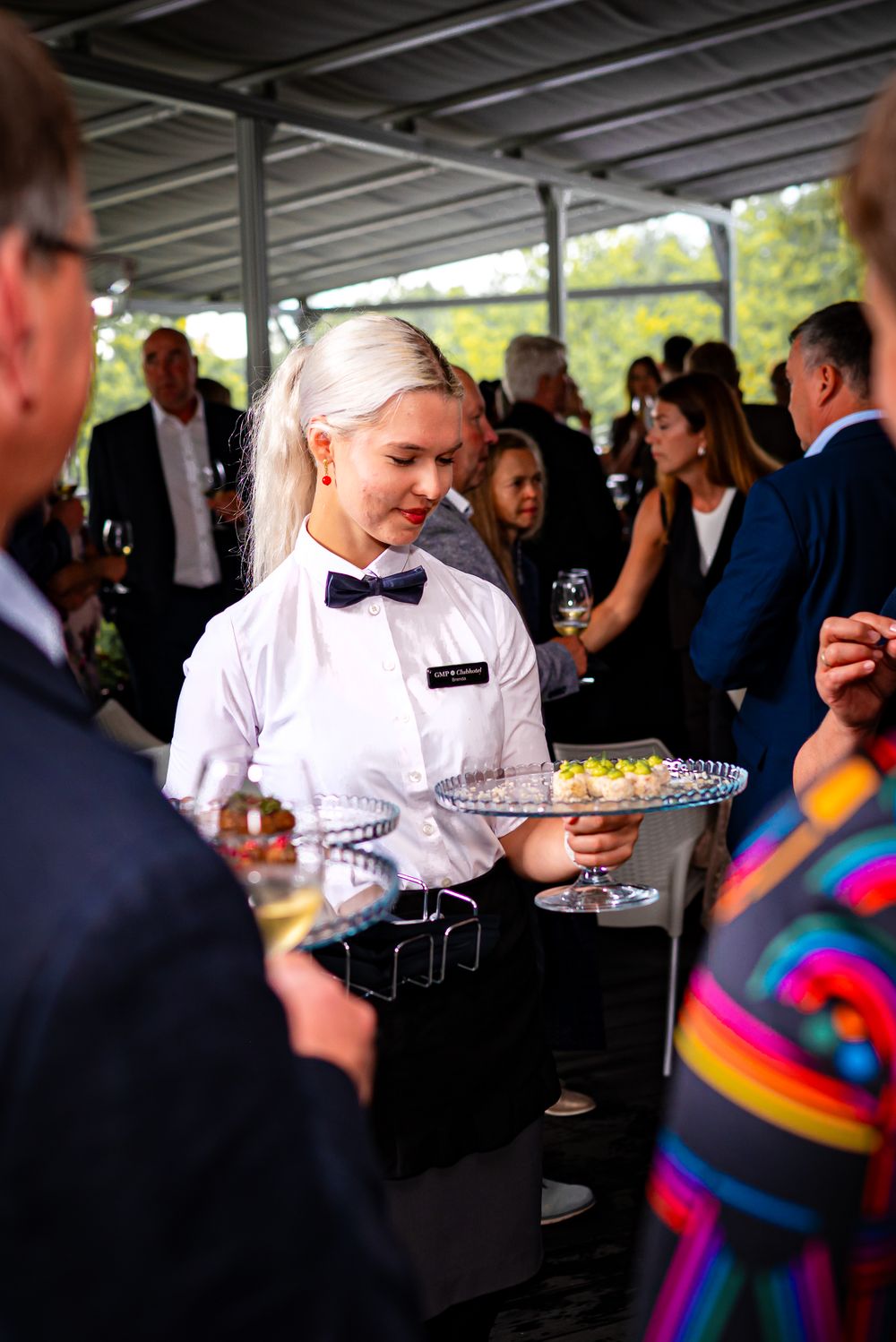 A server in formal attire carries a tray while serving guests at an elegant event.