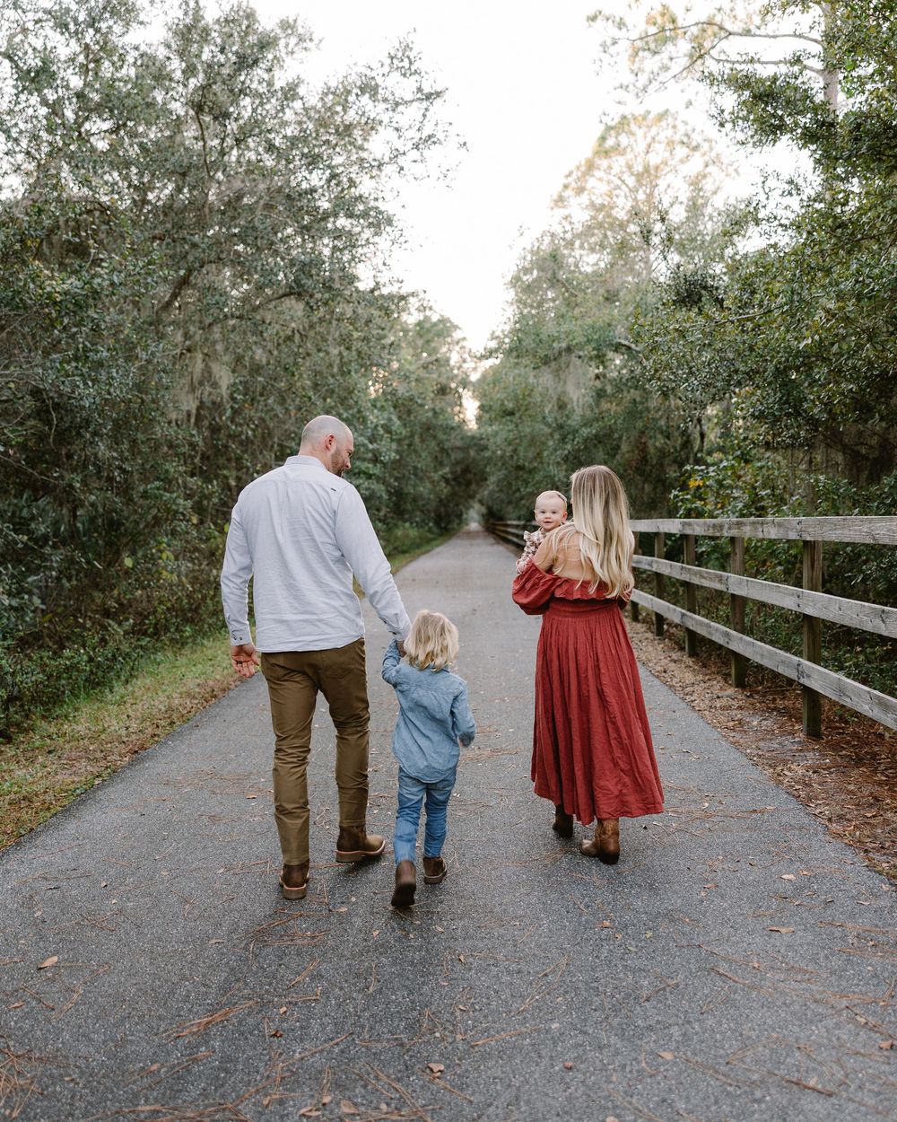 Three people walk together on a tree-lined gravel path on an autumn day.