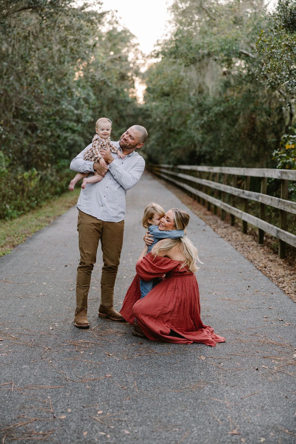 Family enjoying playful moments together on a tree-lined path during golden hour.