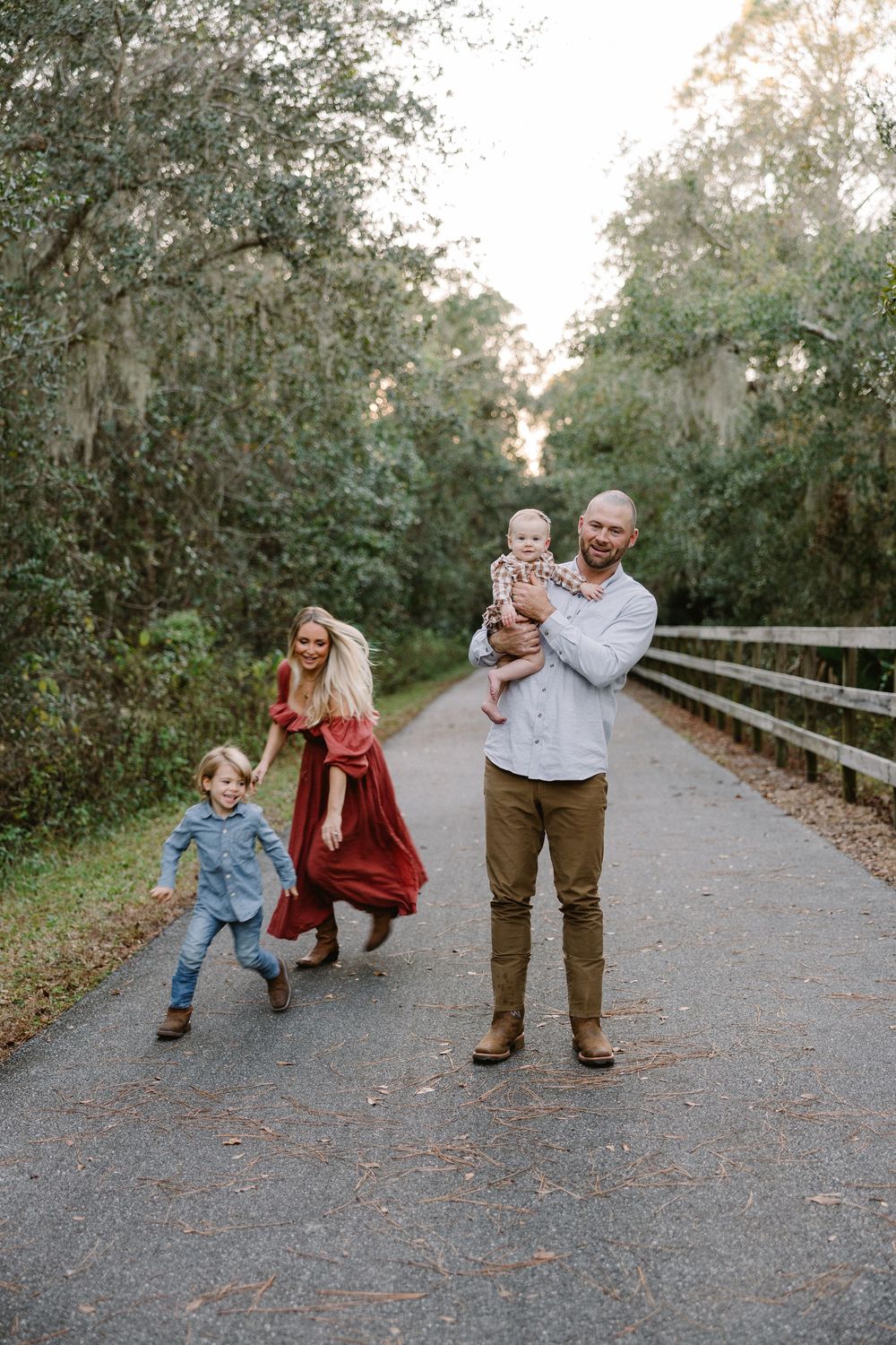 Family enjoying a playful moment together on a tree-lined path with Spanish moss hanging from branches.