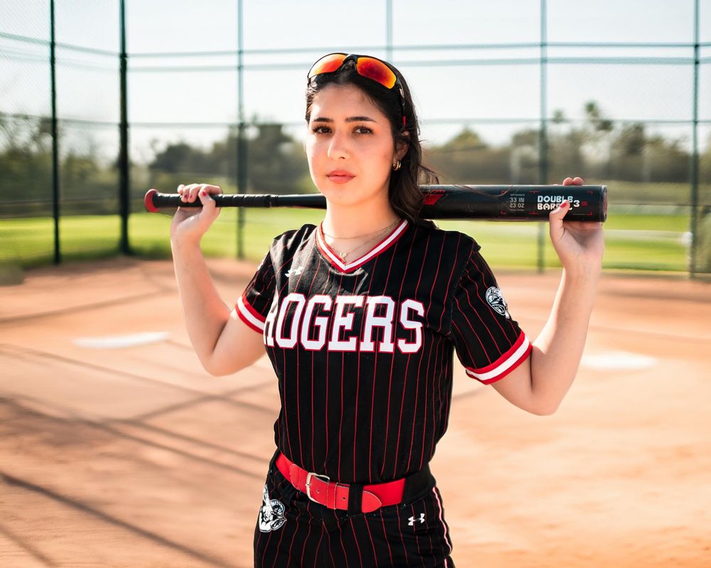 Softball player in pinstripe uniform posing with bat on field.