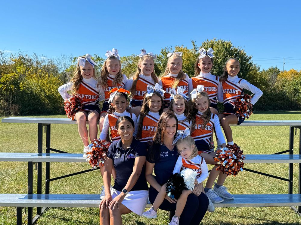 Cheerleaders in red and navy uniforms posing together on bleachers.